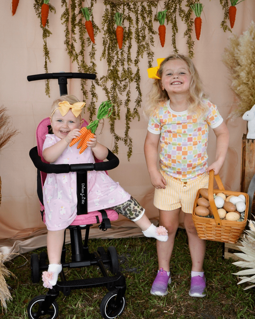 Two blonde girls in Spring-themed outfits smile for a photo while holding Easter-related props