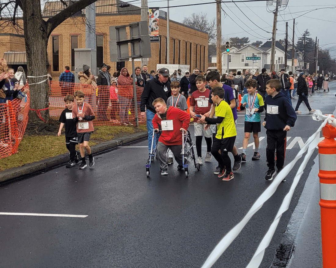 Boy with walker participates in a race while other children cheer him on