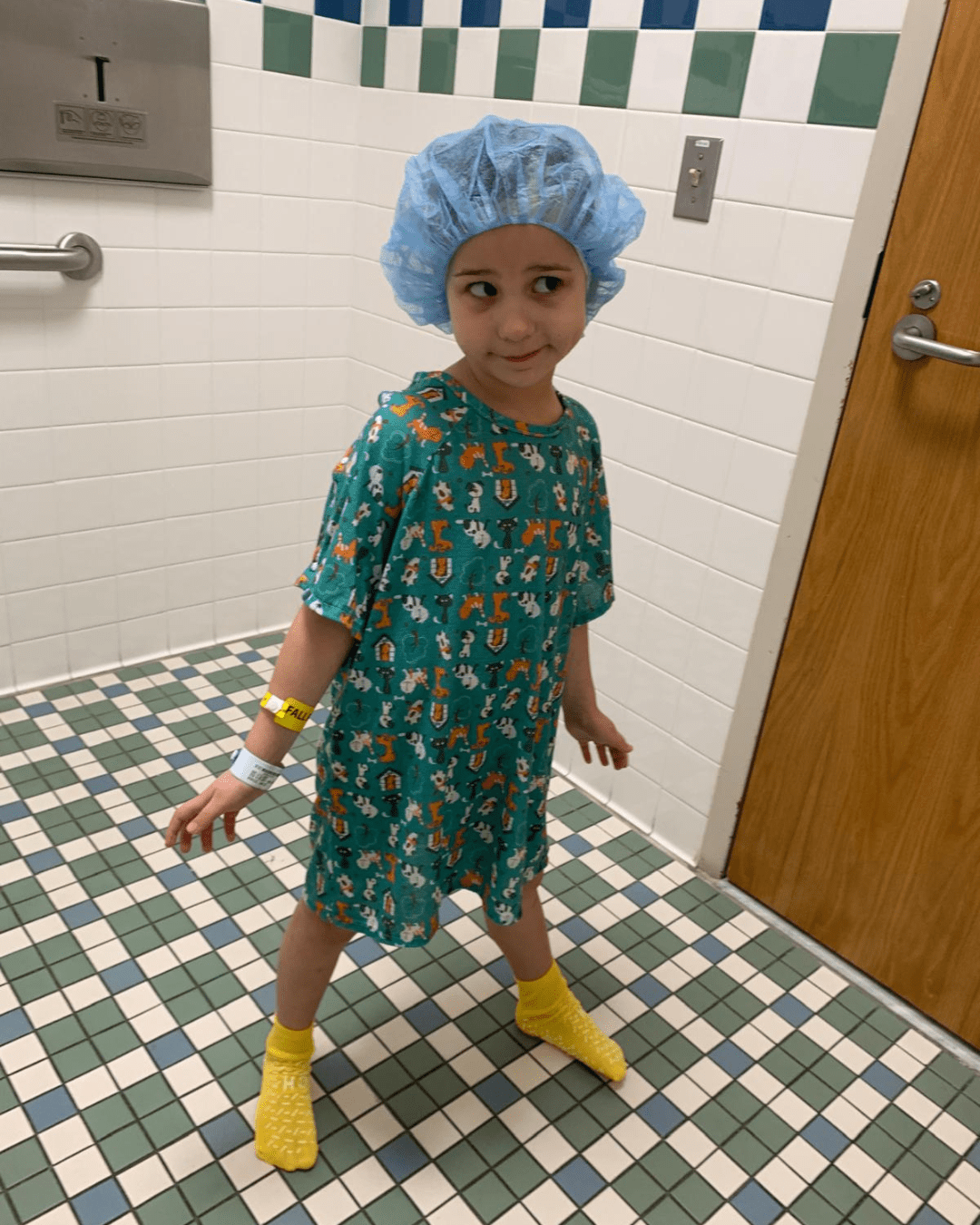 Female child in hospital gown and hair cap poses for a photo in a clinical setting