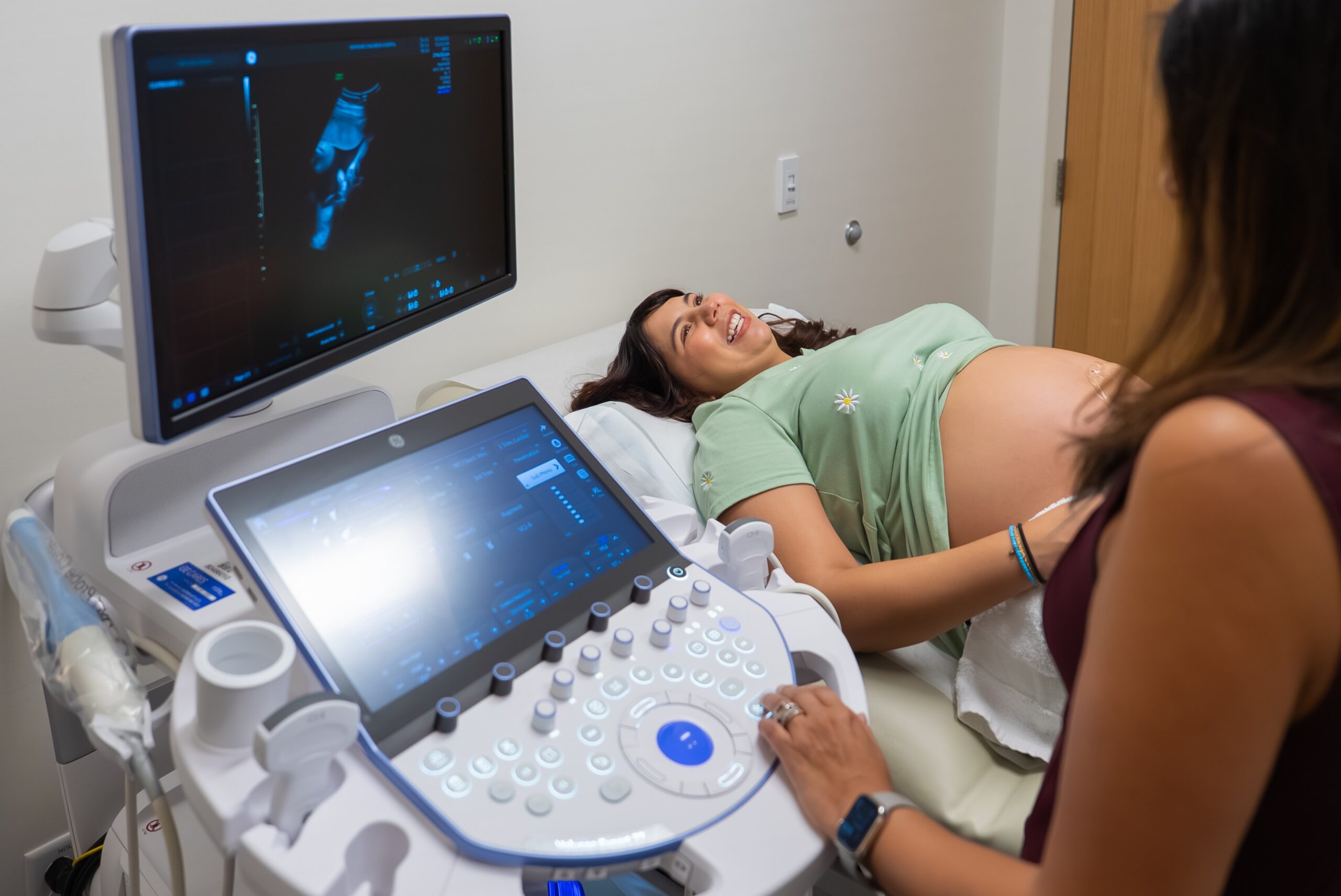 Pregnant woman lays down with a smile while a maternal fetal medicine specialist performs an ultrasound