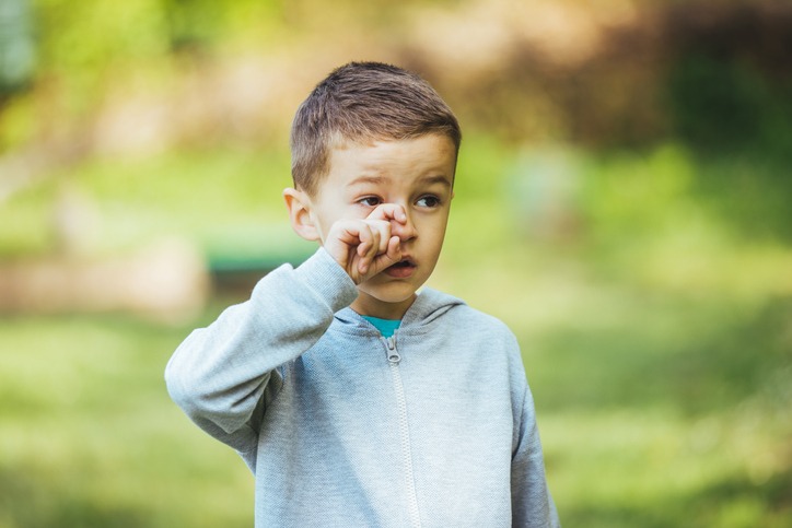 Boy sneezing because of seasonal allergy while sitting in grass during spring.