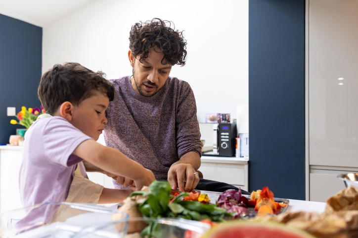 Image of a father and young son preparing fresh vegetables together in a modern kitchen.