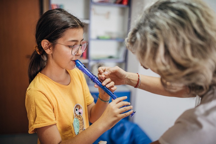 Two people, young girl on music class with female teacher, learning to play flute.