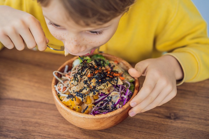 Boy eating Raw Organic Poke Bowl with Rice and Veggies close-up on the table.