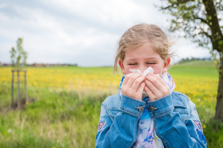 Young girl blowing her nose with closed eyes, suffering from seasonal allergies.