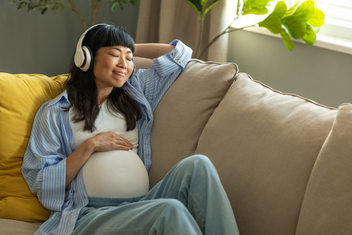 Pregnant woman sitting on sofa and listening music to relax.
