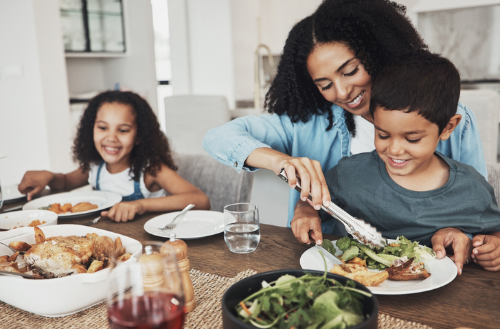 Mom and her children are eating a meal at the table with smiles.