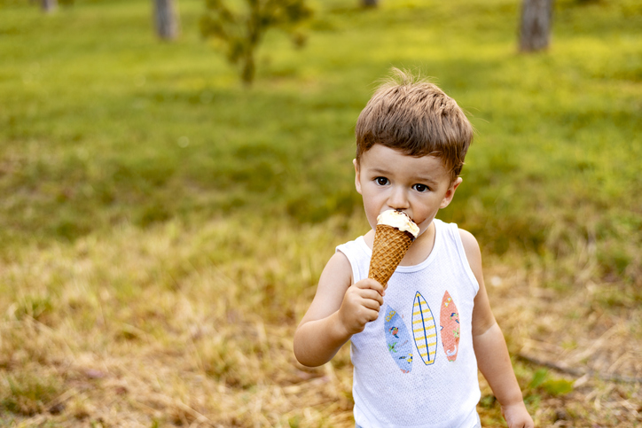Young boy eating ice cream in cone in summer.