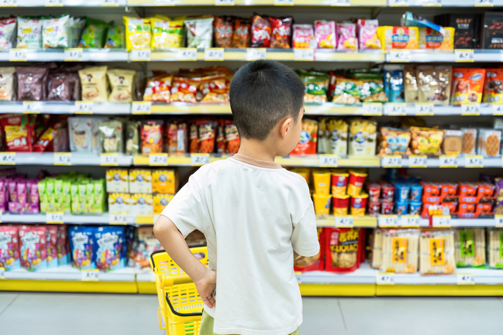 Young boy in a grocery store aisle of cookies and snacks.