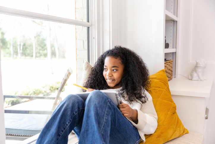 Child sitting by a window drawing in a notebook at home