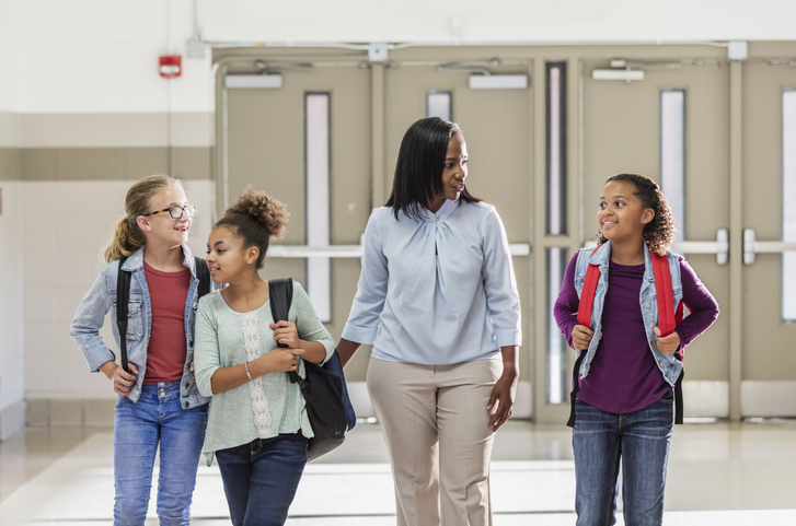 Adult walking with children in a school hallway carrying backpacks
