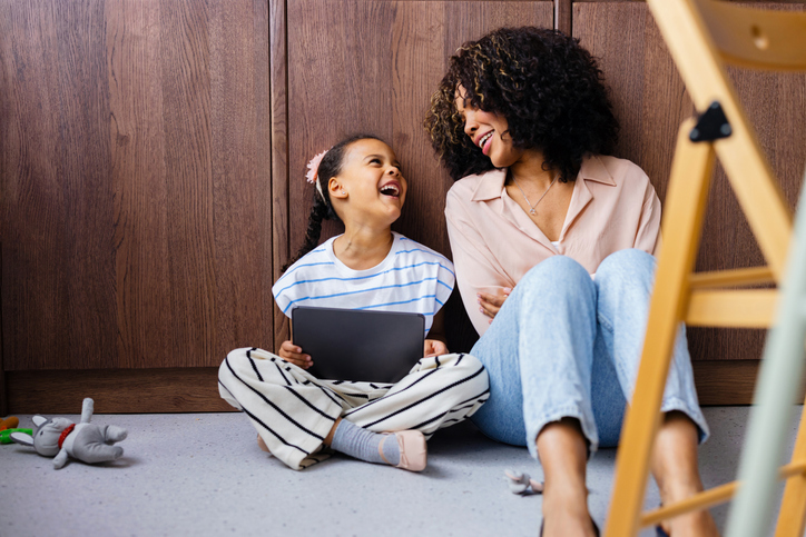 Adult and child sitting together on the floor with a tablet, showing shared interaction alongside technology use
